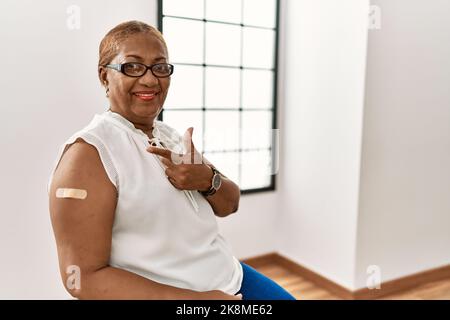 Reife hispanische Frau bekommt Impfstoff zeigt Arm mit Band Hilfe fröhlich mit einem Lächeln auf dem Gesicht zeigt mit Hand und Finger auf die Seite mit glücklich Stockfoto