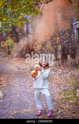 Kleines Mädchen mit Kürbissen im Herbstwald auf verschwommenem Hintergrund Stockfoto