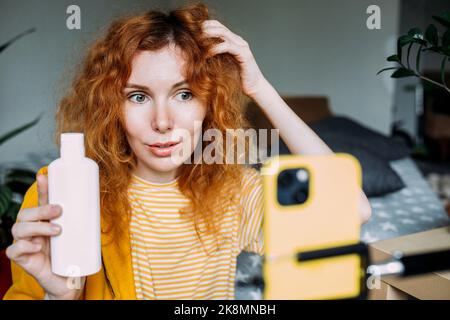 Rothaarige Bloggerin sendet Live-Bewertungen von Schönheitsprodukten für Haare Stockfoto