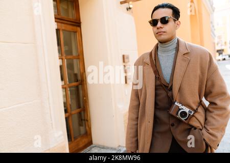 Junger Mann mit Mantel, der seine Hand in der Tasche hält und auf der Stadtstraße läuft Stockfoto