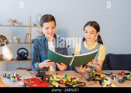 Lächelnde Kinder halten Notebook in der Nähe von Roboter-Modell und Werkzeuge zu Hause, Stock Bild Stockfoto