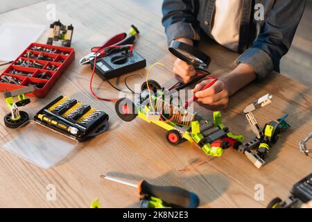 Beschnittene Ansicht eines Jungen, der die Lupe in der Nähe eines Robotermodells und Millimeter auf dem Tisch zu Hause hält, Stockbild Stockfoto