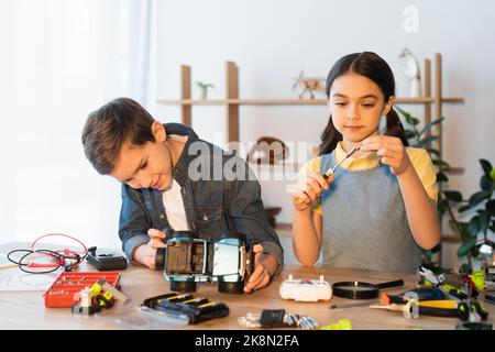 Präteen Mädchen hält Schraubendreher, während junge Montage Auto-Modell in der Nähe von mechanischen Teilen auf dem Tisch, Stock Bild Stockfoto