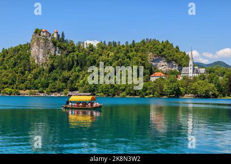 Bled, Slowenien - 18. Juli 2022: Ausflugsboot mit Menschen auf dem Bleder See, unterhalb der Burg von Bled, einem der besten und beliebtesten Touristenattraktionen in Stockfoto