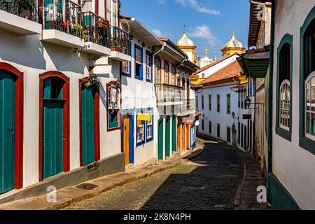 Idyllische Straße mit alten Häusern im Kolonialstil und sonnenbeschienenen Kopfsteinpflastern in der historischen Stadt Ouro Preto in Minas Gerais Stockfoto