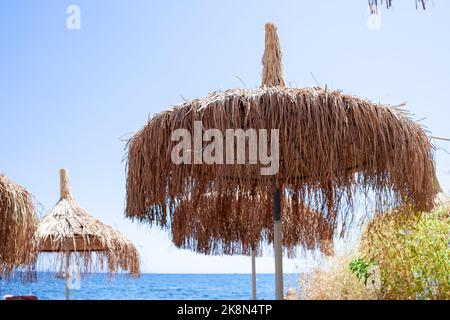 Strohschirm oder Strohhütte mit wunderschönem Blick auf den tropischen Strand. Strohschirme am Strand gegen klaren blauen Himmel Stockfoto