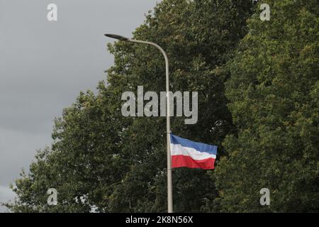 Eine umgekehrte niederländische Flagge, die an einem Laternenpfosten hängt und gegen die Blätter eines Baumes eingefangen wurde Stockfoto