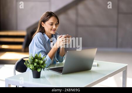 Schöne junge Brünette Frau mit Laptop während der Arbeit zu Hause trinkt Kaffee. Stockfoto