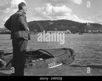 Oslo. 19490715. Ein Mann steht auf dem Rocker mit einer Zigarette im Mund. Im Hintergrund sind Ekebergåsen und Bekkelaget mit der Seamen's School T.H und dem kleineren Ekebergrestaurant T. v. im Bild zu sehen. Grønlikaia mit großem Lager und Operationshalle. Krane und verschiedene Arten von Booten charakterisieren das Thema ebenfalls. Foto: NTB Stockfoto