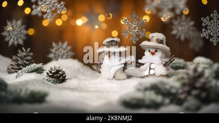 Weihnachtsszene mit Schneemann und hängenden Ornamenten, Holzhintergrund und Schnee, die beleuchteten braunen Bretter und Lichter schaffen eine festlich warme Stimmung Stockfoto