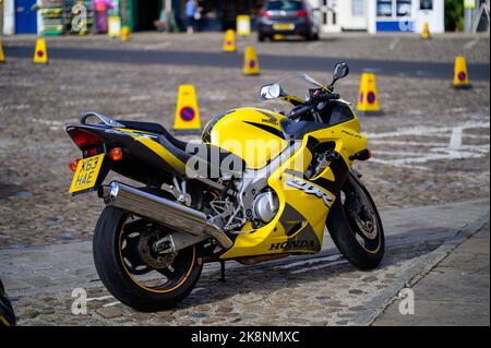 Richmond, North Yorkshire, Großbritannien - 3. August 2020: Gelbes Motorrad auf dem gepflasterten Richmond Market Place. Verkehrskegel im Hintergrund außer Fokus Stockfoto