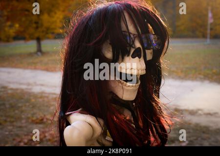 Aus der Nähe eines weiblichen Skeletts auf einem Motorrad mit schönen Herbstfarben und Flagge im Hintergrund sitzen Stockfoto