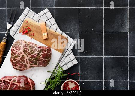 Steaks Raw. Rohes Cowboy-Steak, marmoriertes Rindfleisch mit Gewürzen Rosmarin und Pfeffer auf weißem Marmorschiefer und grauem Tischhintergrund. Draufsicht. Modell. Stockfoto