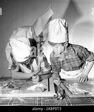 Oslo Weihnachten 1958. Kinder backen Lebkuchen. Eines Tages während der Weihnachtszeit interessierten sich die Jungen der Mutter plötzlich für häusliche Aktivitäten und begannen, die Küche zu benutzen, die den Mädchen vorbehalten war. Drei Brüder werden zu Weihnachten Lebkuchenmänner machen. Ein Bäcker ist kein Bäcker ohne Schürze und Backhut Papa's Shirt und eine weiße Papiertüte hat den Dienst getan. Das Ergebnis des Backens war so erfolgreich, dass kein Lebkuchen in die Box kam. Sie gingen im Magen der Bäcker. Hier haben die Bäcker Probleme mit dem Teig, der am Tisch klebt. Foto: Aage Storløkken NTB / NTB Stockfoto