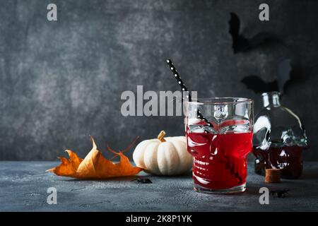 Blutiger Halloween-Cocktail. Blutig roter Cocktailglas-Becher für Halloween und Flaschenform Totenkopf auf dunklen Hintergründen. Halloween-Party mit Süßigkeiten Augen, Stockfoto