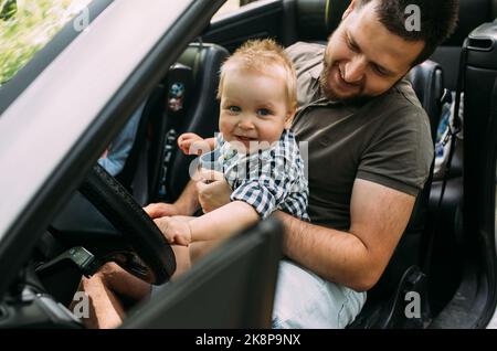 Papa zeigt seinem kleinen Sohn, wie er das Auto fährt, während er hinter dem Steuer sitzt Stockfoto