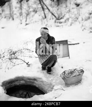 Hedmark im Winter 1948. Wasserknappheit in Ostnorwegen nach der Dürre im Sommer 1947. Die Betriebe müssen Wasser in den Flüssen holen oder Wasser aus den Molkereien fließen lassen. Hier wäscht eine Frau die Kleidung in einem Bach, durch ein Loch, das im Eis gehackt wird. Es ist kalt und die Frau wärmt ihre Hände, indem sie sie bläst. BALL mit Kleidung und Waschbrett. Foto: Børretzen / Aktuell / NTB Stockfoto