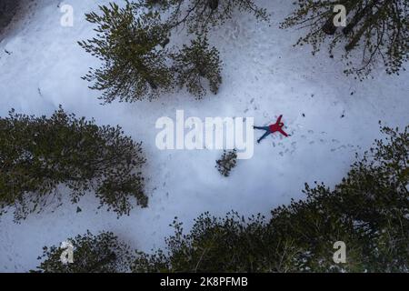 Drohnenantenne einer Frau in warmer Kleidung legt sich im Winter bei Neuschnee Stockfoto