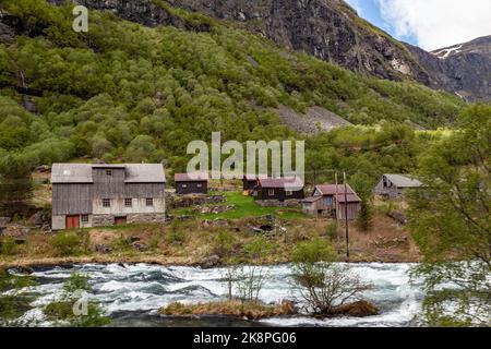 Ein Fluss vor alten Häusern mit Wäldern und hohen Bergen im Hintergrund Stockfoto