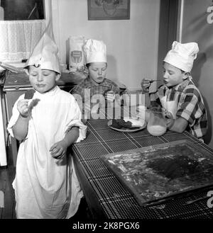 Oslo Weihnachten 1958. Kinder backen Lebkuchen. Eines Tages während der Weihnachtszeit interessierten sich die Jungen der Mutter plötzlich für häusliche Aktivitäten und begannen, die Küche zu benutzen, die den Mädchen vorbehalten war. Drei Brüder werden zu Weihnachten Lebkuchenmänner machen. Ein Bäcker ist kein Bäcker ohne Schürze und Backhut. Das Hemd des Vaters und eine weiße Papiertüte waren der Service. Das Ergebnis des Backens war so erfolgreich, dass kein Lebkuchen in die Box kam. Sie gingen im Magen der Bäcker. Foto: Aage Storløkken NTB / NTB Stockfoto