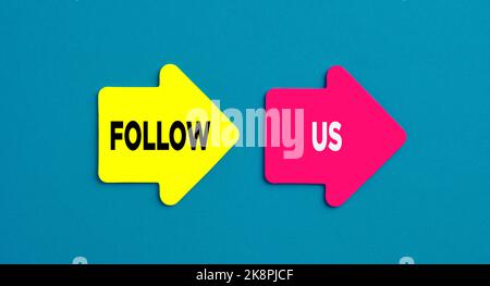 Folgen Sie uns Konzept. Das Wort folgt uns auf pfeilförmigen Aufklebern auf blauem Hintergrund. Stockfoto