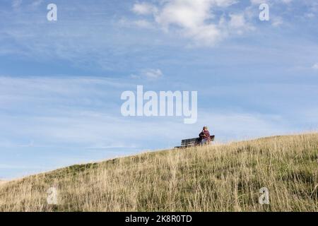 Frau sitzt allein auf einer Bank tief in Gedanken unter blauen Sommer-Skys, kopieren Raum, Einsamkeit Konzept Stockfoto