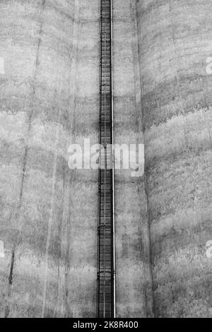 Eine schwarz-weiße Aufnahme einer Leiter, die eine Betonwand eines Fabriksilos in Toten, Norwegen, hinaufführt Stockfoto
