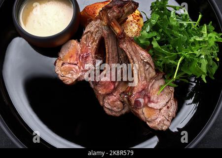 Gegrillte Lammrippen auf einem Teller, mit Sauce und Kräutern Stockfoto