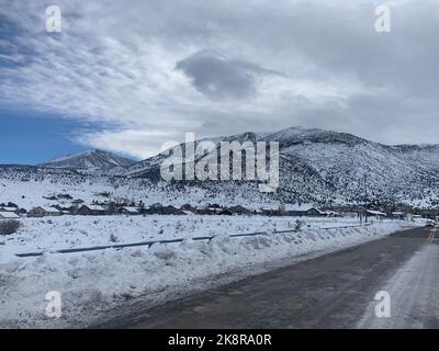 Eine alte Asphaltstraße zwischen verschneiten Tälern und Bergen in Mammoth Lakes Town, Kalifornien Stockfoto