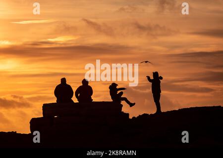 Portland, Dorset, Großbritannien. 24. Oktober 2022. Besucher trotzen den wehenden Meereswinden, um den Sonnenuntergang in Portland Bill in Dorset an einem unSaison warmen Tag in Südengland zu sehen. Kredit: Peter Lopeman/Alamy Live Nachrichten Stockfoto