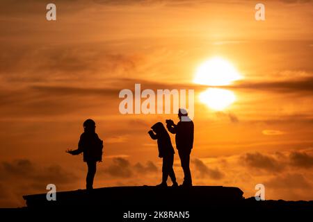 Portland, Dorset, Großbritannien. 24. Oktober 2022. Besucher trotzen den wehenden Meereswinden, um den Sonnenuntergang in Portland Bill in Dorset an einem unSaison warmen Tag in Südengland zu sehen. Kredit: Peter Lopeman/Alamy Live Nachrichten Stockfoto