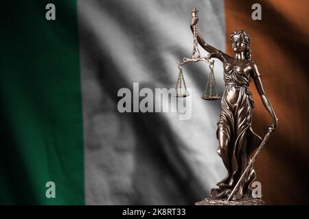 Irische Flagge mit Statue der Justizdame und Justizwaagen in dunklem Raum. Konzept von Urteil und Bestrafung, Hintergrund für Jurythemen Stockfoto