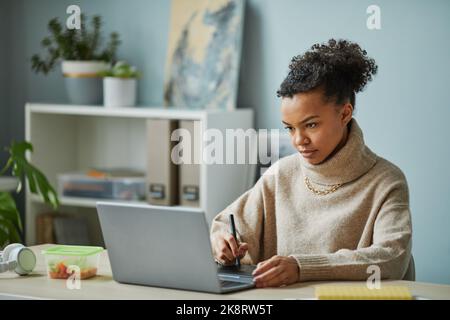 Afrikanischer junger Designer, der mit einem grafischen Tablet am Tisch im Büro an der Erstellung einer Website arbeitet Stockfoto