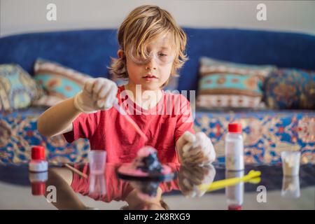 Kind Junge tun chemische Experiment zu Hause. Kinder mit Schutzbrille untersuchen Pipettentropfflüssigkeit in Reagenzgläser, Kaukasisch und Biochemie Stockfoto