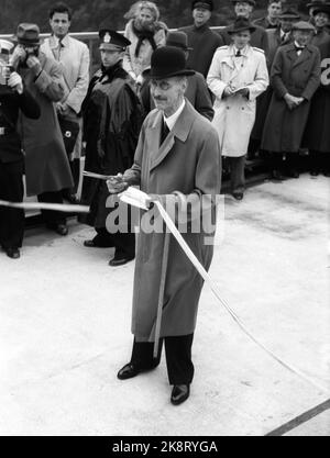 Svinesund 19460615. Die Svinesundbrücke in Halden zwischen Norwegen und Schweden wird von König Haakon und Kronprinz Gustav Adolf inmitten der 420 Meter langen Brücke eröffnet. König Haakon bereitet mit der vergoldeten Schere vor, dass er das Seidenband in Rot-Weiß-Blau schneiden wird. Mantel, Hut und Stock. Foto: Current / NTB Stockfoto