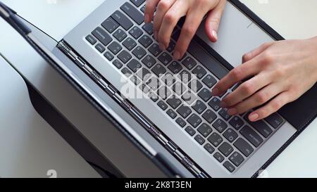 In Nahaufnahme tippen Frauenhände etwas auf einer grauen Laptop-Tastatur auf einem weißen Desktop. Hochwertige Fotos Stockfoto