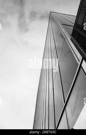 Eine vertikale Graustufenaufnahme eines modernen Glasgebäudes gegen den bewölkten Himmel Stockfoto