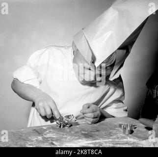 Oslo Weihnachten 1958. Kinder backen Lebkuchen. Eines Tages während der Weihnachtszeit interessierten sich die Jungen der Mutter plötzlich für häusliche Aktivitäten und begannen, die Küche zu benutzen, die den Mädchen vorbehalten war. Drei Brüder werden zu Weihnachten Lebkuchenmänner machen. Ein Bäcker ist kein Bäcker ohne Schürze und Backhut Papa's Shirt und eine weiße Papiertüte hat den Dienst getan. Das Ergebnis war so erfolgreich, dass keine Lebkuchen in der Box landeten. Sie gingen im Magen der Bäcker. Die Gesichter bekamen mehr Runden mit Mehl als mit Leiben. Foto: Aage Storløkken NTB / NTB Stockfoto