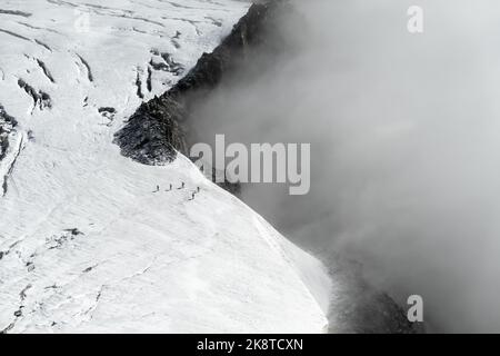Chamonix, Frankreich - 31. August 2022: 5 Wanderer auf dem Glacier du Geant im Mont-Blanc-Massiv, die sich von der Klippe entfernen, während sich Wolken bewegen Stockfoto