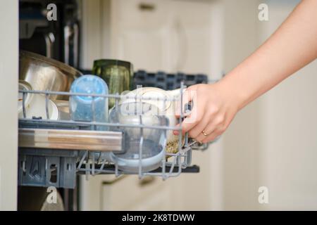 Eine weibliche Hand öffnet ein Spülmaschinentablett mit Tassen und Tellern, Nahaufnahme Stockfoto