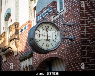 Eine große alte Uhr hängt an der Außenwand eines Gebäudes. Vintage Design-Objekt auf einer roten Ziegelwand. Die alte Stahluhr zeigt die Zeit an. Stockfoto