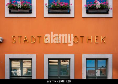 Beschriftung der Stadtbibliothek auf der Außenseite des Gebäudes. Goldene Buchstaben auf einer orangefarbenen Fassade. Ein Service zum Ausleihen von Büchern in einer Stadt. Stockfoto
