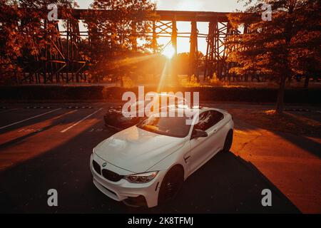 Vorderansicht eines modernen weißen BMW M4 und eines schwarzen Audi RS5 bei Sonnenuntergang auf der Straße. Luxuriöse Sportwagen Stockfoto