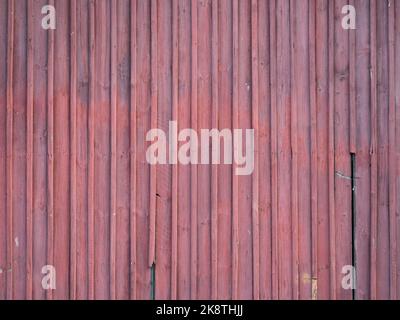 Rote Holzplanken Hintergrund. Teilweise gebrochene und verwitterte Bretter. Struktur eines Gebäudes außerhalb eines alten Hauses. Ein vertikales Muster. Stockfoto