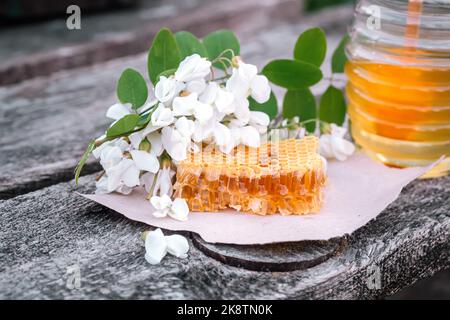 Honig im Glas mit Akazienblüten auf rustikalem Holzhintergrund. Golden, frisch. Stockfoto