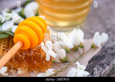 Honey Dipper , liegt Honey Stick auf Stück abgeschnitten frischen Honig in Waben. Akazienhonig in gar auf Holzgrund. Frühlingsstimmung. Selektiver Fokus. Stockfoto