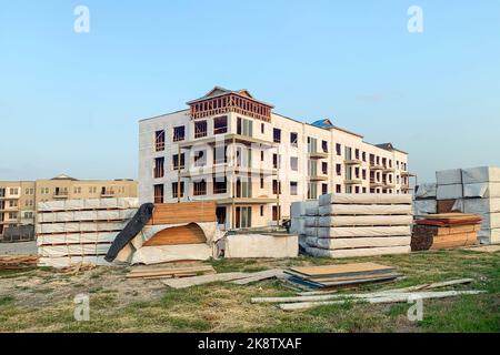 Ein unvollendetes Gebäude eines mehrstöckigen Gebäudes, ein Haus im Bau, das von einer großen Menge Holz und anderen Hölzern umgeben ist. Stockfoto