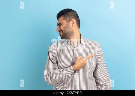 Raus. Porträt eines ernsten, wütenden Geschäftsmannes, der mit dem Finger zeigt, schleichen einen Mann, der andere Menschen beschuldigt, sich ins Gesicht dreht und gestreiftes Hemd trägt. Innenaufnahme des Studios isoliert auf blauem Hintergrund. Stockfoto