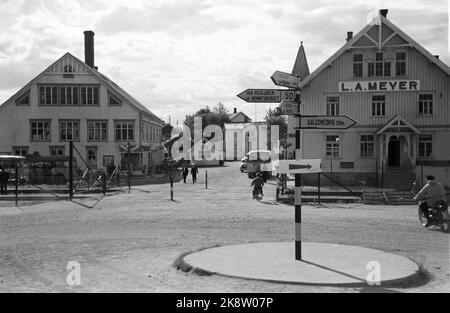 Rana 19520906: 'Abenteuerliche Dimensionen'. Die in Mo i Rana gebaute Eisenhütte ist nicht nur Norwegens größtes Unternehmen, sie ist auch eine ziemlich umstrittene Maßnahme. Die Umsetzung der schmiedeeisernen Pläne hat in unserer öffentlichen Diskussion starke Wellen ausgelöst. Bild: Rana Zentrum. T.H. Auf dem Bild L. A. Meyer (Meyergården). In der Mitte des Bildes Fish Trade und Central Café. Busse. Im Vordergrund Kreisverkehr mit Wegweisern nach Bodø, Rognan, Mosjøen, Hemnesberget und Guldsmedvik. Foto: Sverre A. Børretzen / Aktuell / NTB Stockfoto