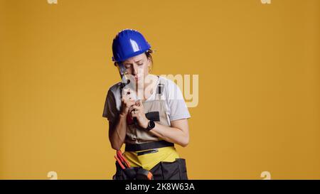Porträt einer mächtigen Bauherrin, die bei Bauarbeiten Kopfschmerzen hat und Hammer hält, um Schläfen zu reiben. Überarbeitete kranke Frau, die im Studio an Schmerzen und Migräne litt. Stockfoto